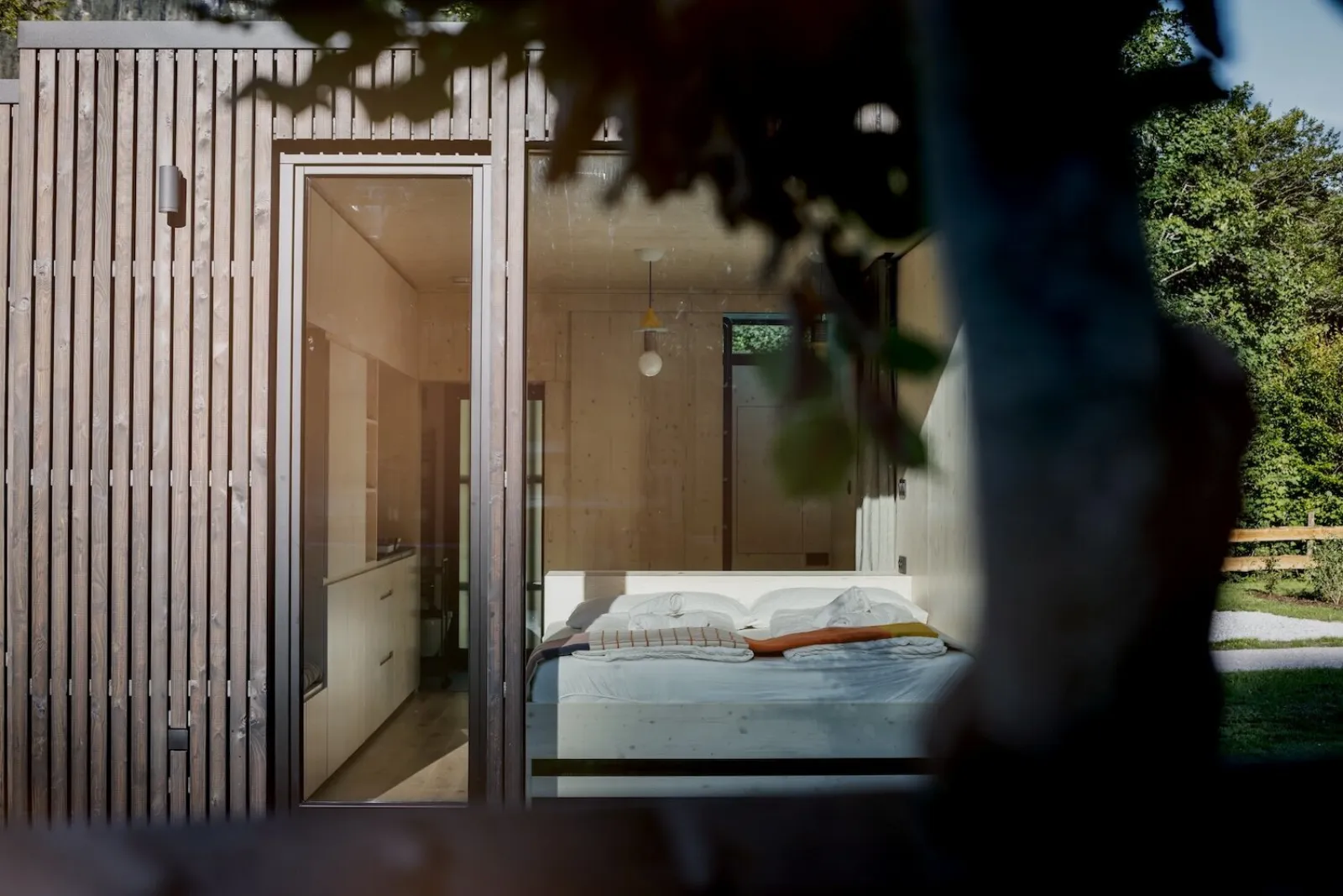 Ein einzelnes Tiny Home mit großer Glasfront, dahinter ein gemachtes Bett mit Blick ins Grüne